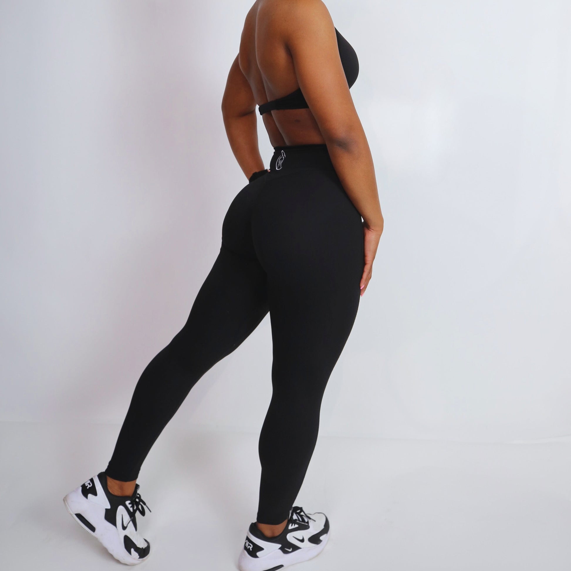A model wearing high-waist black leggings with a cinched waist with aesthetic trim detailing.